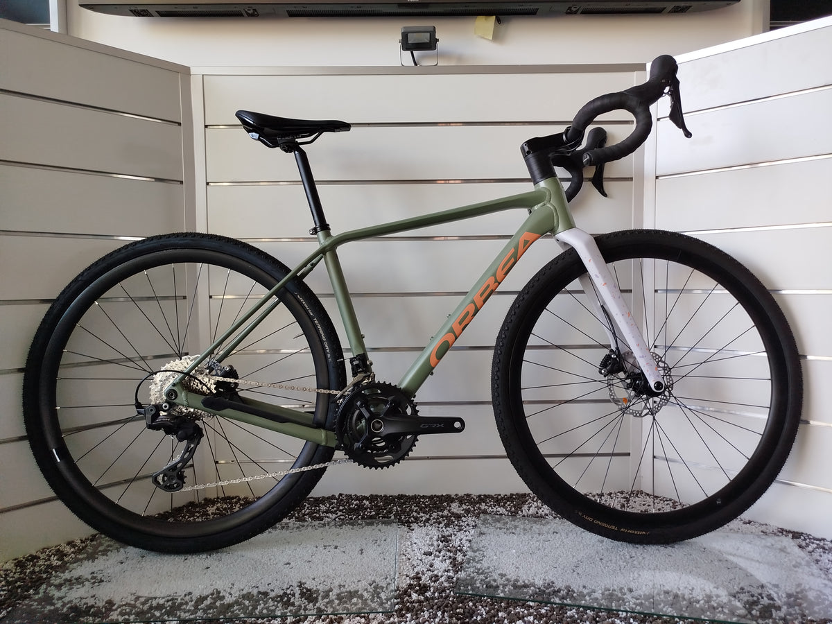 Bicicletta gravel Orbea Terra H30 in colorazione Infinity Green lucido con dettagli Ivory White. Inquadratura laterale del telaio in alluminio idroformato a triplo spessore e forcella in carbonio con passaggio cavi integrato ICR. Visibili il gruppo Shimano GRX a 12 velocità, i freni a disco idraulici e i pneumatici tassellati da gravel.