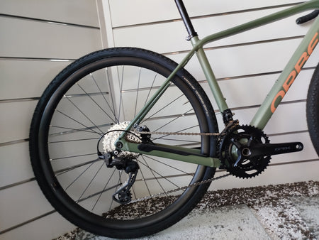Bicicletta gravel Orbea Terra H30 in colorazione Infinity Green lucido con dettagli Ivory White. Inquadratura laterale del telaio in alluminio idroformato a triplo spessore e forcella in carbonio con passaggio cavi integrato ICR. Visibili il gruppo Shimano GRX a 12 velocità, i freni a disco idraulici e i pneumatici tassellati da gravel.
