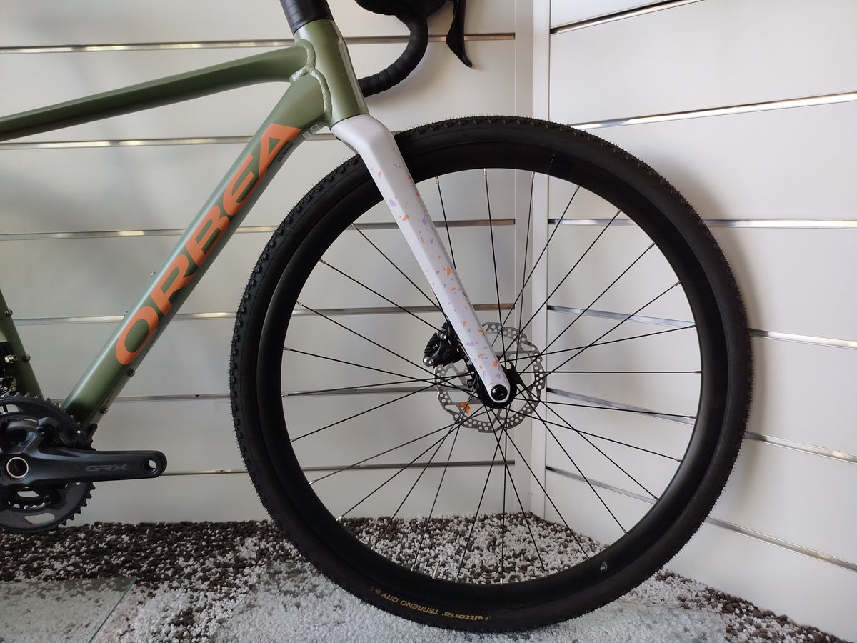 Bicicletta gravel Orbea Terra H30 in colorazione Infinity Green lucido con dettagli Ivory White. Inquadratura laterale del telaio in alluminio idroformato a triplo spessore e forcella in carbonio con passaggio cavi integrato ICR. Visibili il gruppo Shimano GRX a 12 velocità, i freni a disco idraulici e i pneumatici tassellati da gravel.