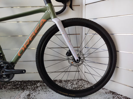 Bicicletta gravel Orbea Terra H30 in colorazione Infinity Green lucido con dettagli Ivory White. Inquadratura laterale del telaio in alluminio idroformato a triplo spessore e forcella in carbonio con passaggio cavi integrato ICR. Visibili il gruppo Shimano GRX a 12 velocità, i freni a disco idraulici e i pneumatici tassellati da gravel.